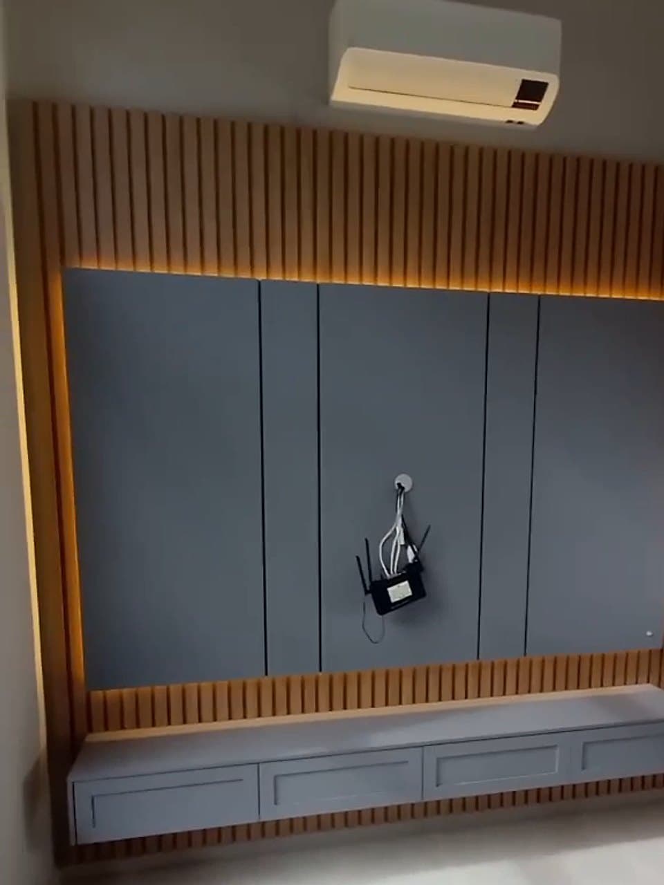 O mesmo painel instalado, com ripado de madeira, LED aceso e rack suspenso